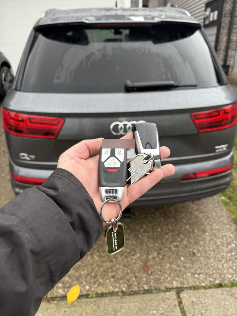 Hand holding Audi key fobs behind a grey Audi Q7 in Vancouver
