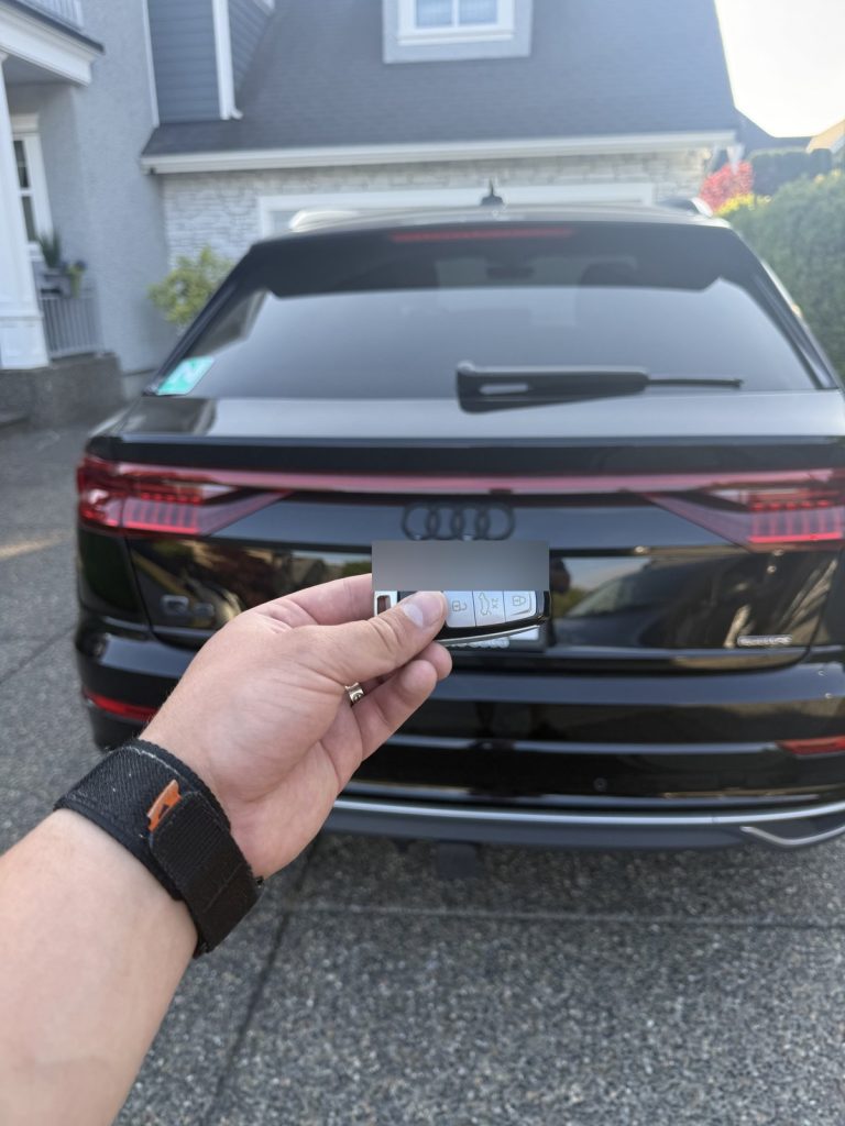 Hand holding an Audi key fob behind a black Audi Q8 in a Vancouver driveway