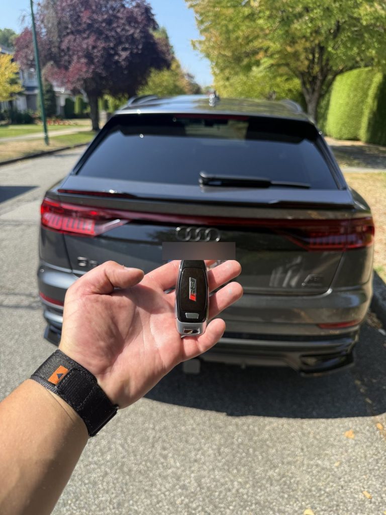 Hand holding an Audi smart key behind a grey Audi Q8 on a Vancouver street