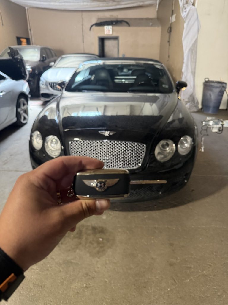 Hand holding a Bentley key fob in front of a black Bentley in a Vancouver garage