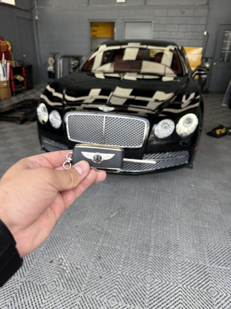 Hand holding a Bentley smart key in front of a black Bentley in a Vancouver garage