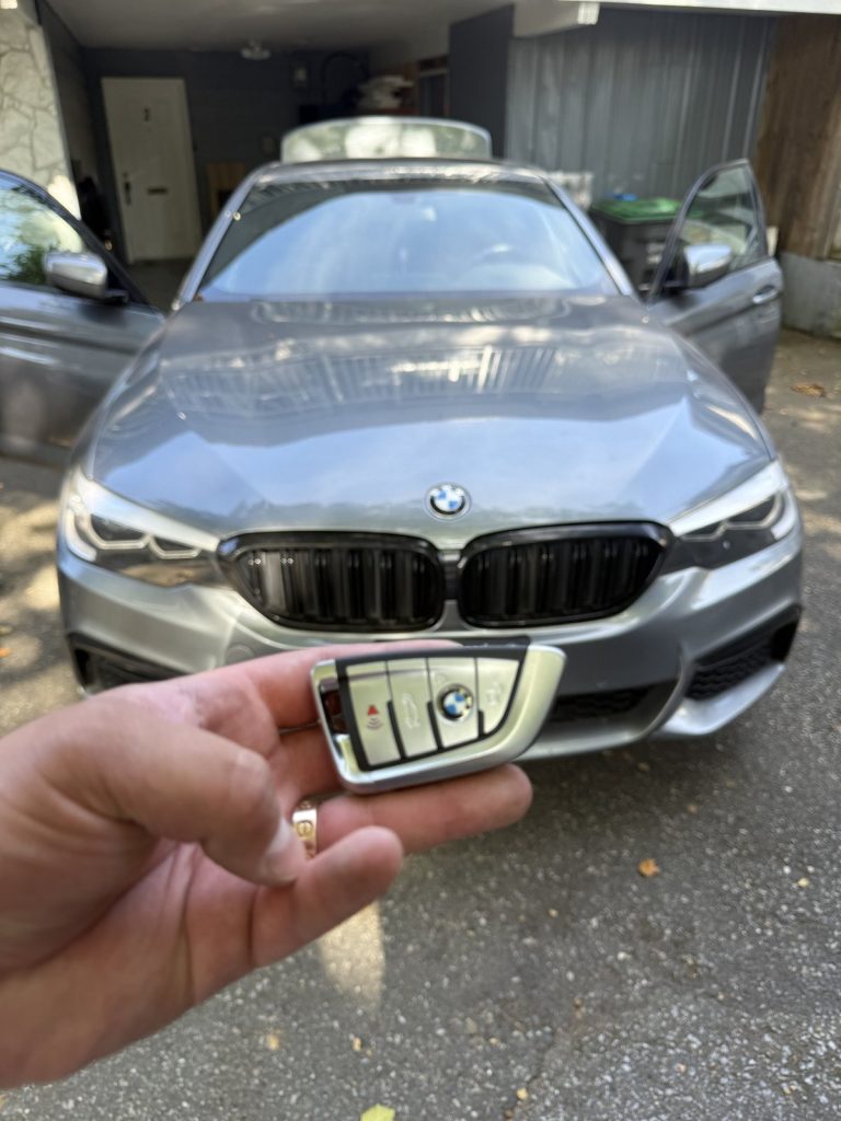 Hand holding a BMW smart key in front of a grey BMW 5 Series in Vancouver
