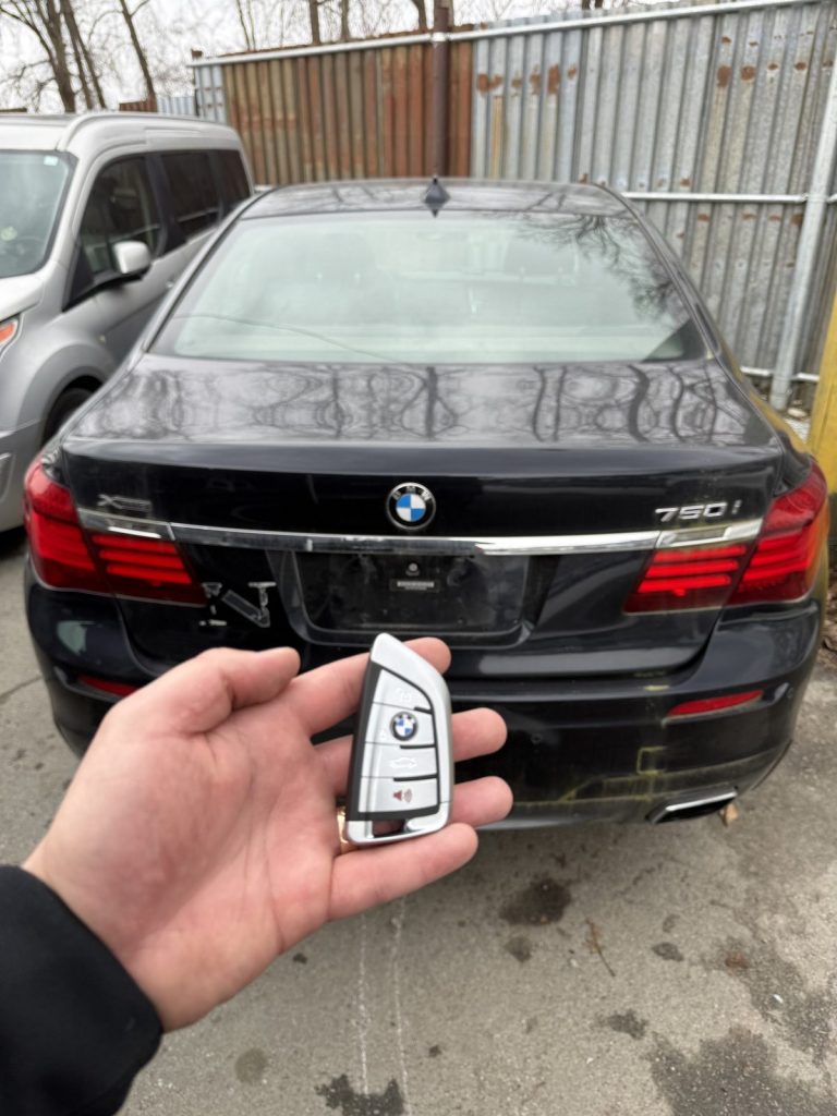 Hand holding a BMW smart key behind a black BMW 750i in Vancouver