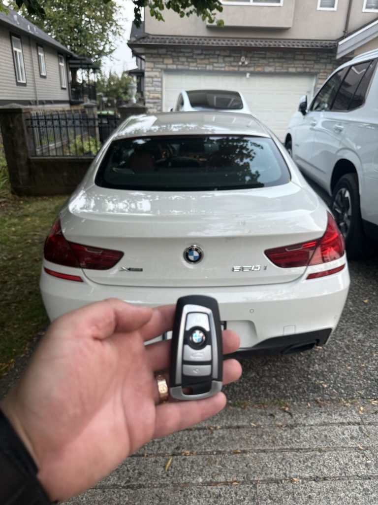 Hand holding a BMW smart key behind a white BMW coupe in Vancouver