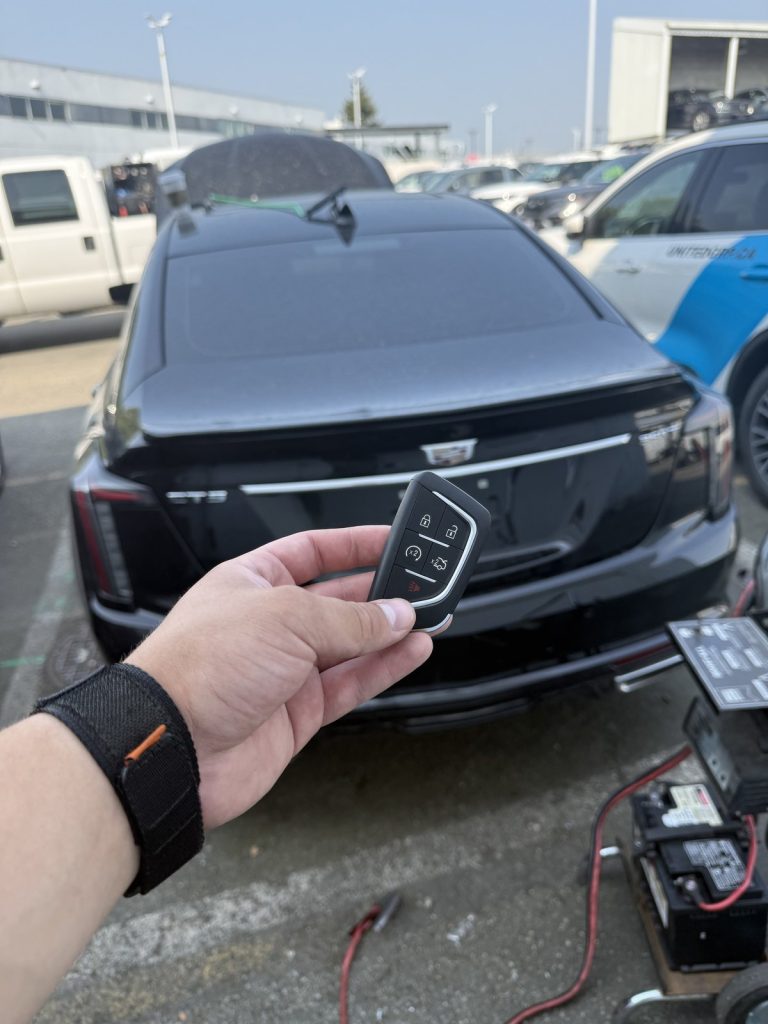 Hand holding a Cadillac smart key behind a black Cadillac sedan with a battery pack on the ground in Vancouver