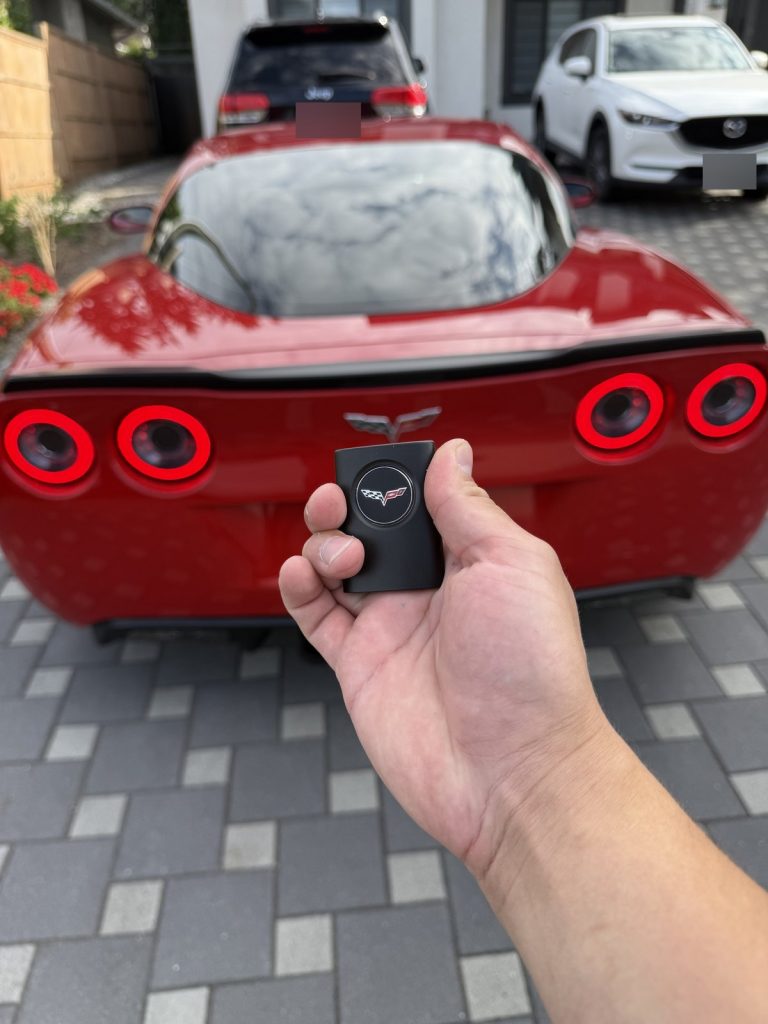 Hand holding a Corvette key fob behind a red Chevrolet Corvette in Vancouver