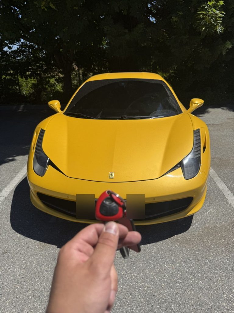 Hand holding a Ferrari key in front of a yellow Ferrari 458 in Vancouver