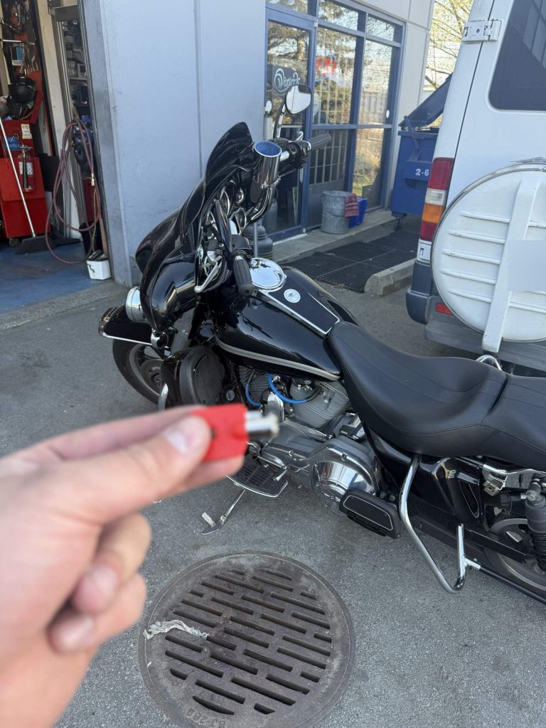 Hand holding a red-headed motorcycle key beside a black Harley-Davidson touring motorcycle in Vancouver