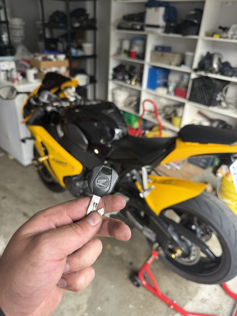 Hand holding a Honda motorcycle key in front of a yellow Honda sport motorcycle in a Vancouver garage