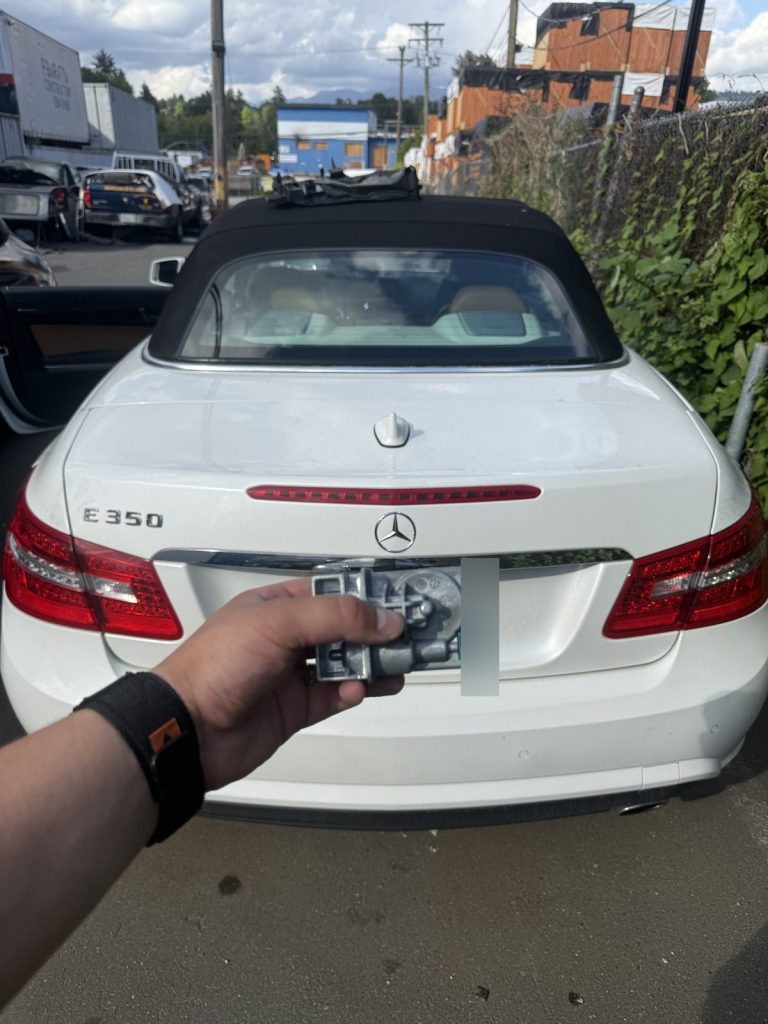 Hand holding an electronic lock module behind a white Mercedes-Benz E350 convertible in Vancouver