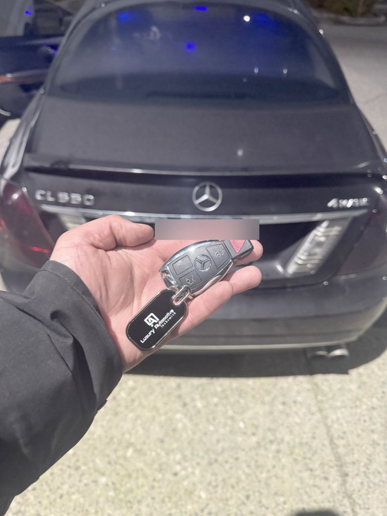 Hand holding a Mercedes-Benz key fob on a Luxury Automotive Locksmith key tag behind a Mercedes-Benz sedan in Vancouver