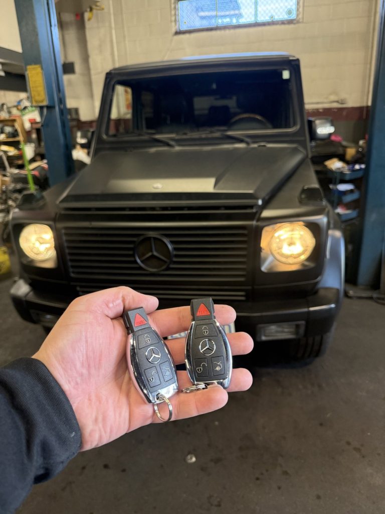 Hand holding two Mercedes-Benz key fobs in front of a black Mercedes-Benz G-Class in a Vancouver garage