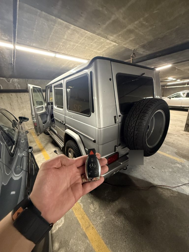 Hand holding a Mercedes-Benz key fob beside a silver Mercedes-Benz G-Class in a Vancouver parkade