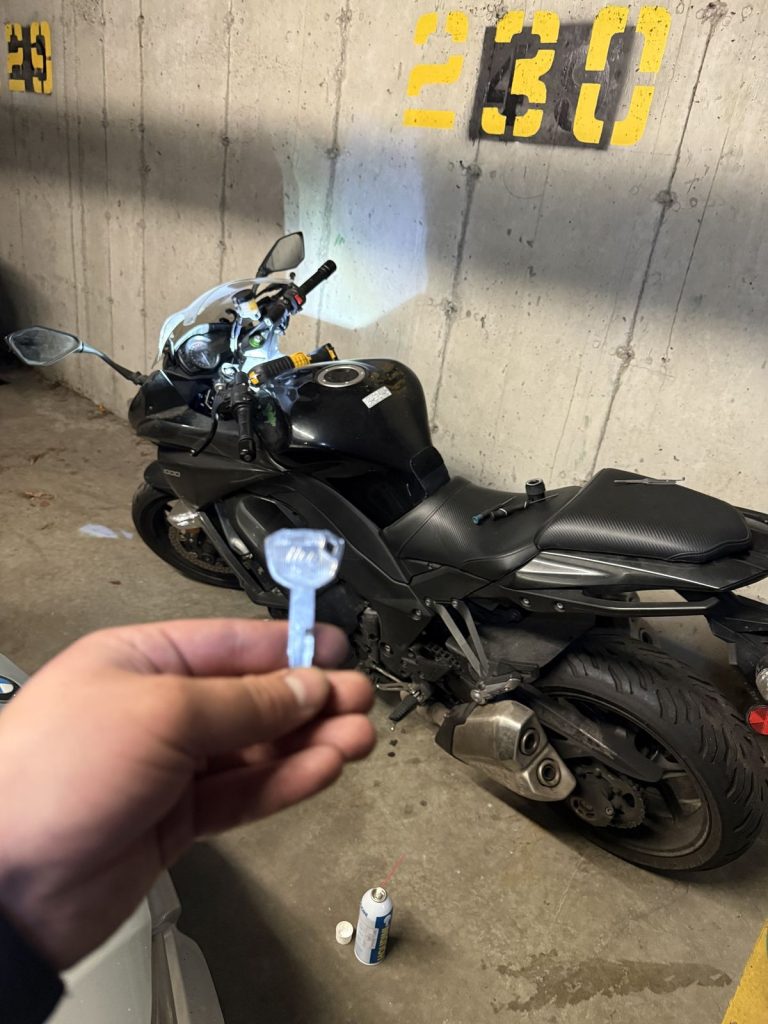 Hand holding a motorcycle key beside a black sport-touring motorcycle in a Vancouver parkade