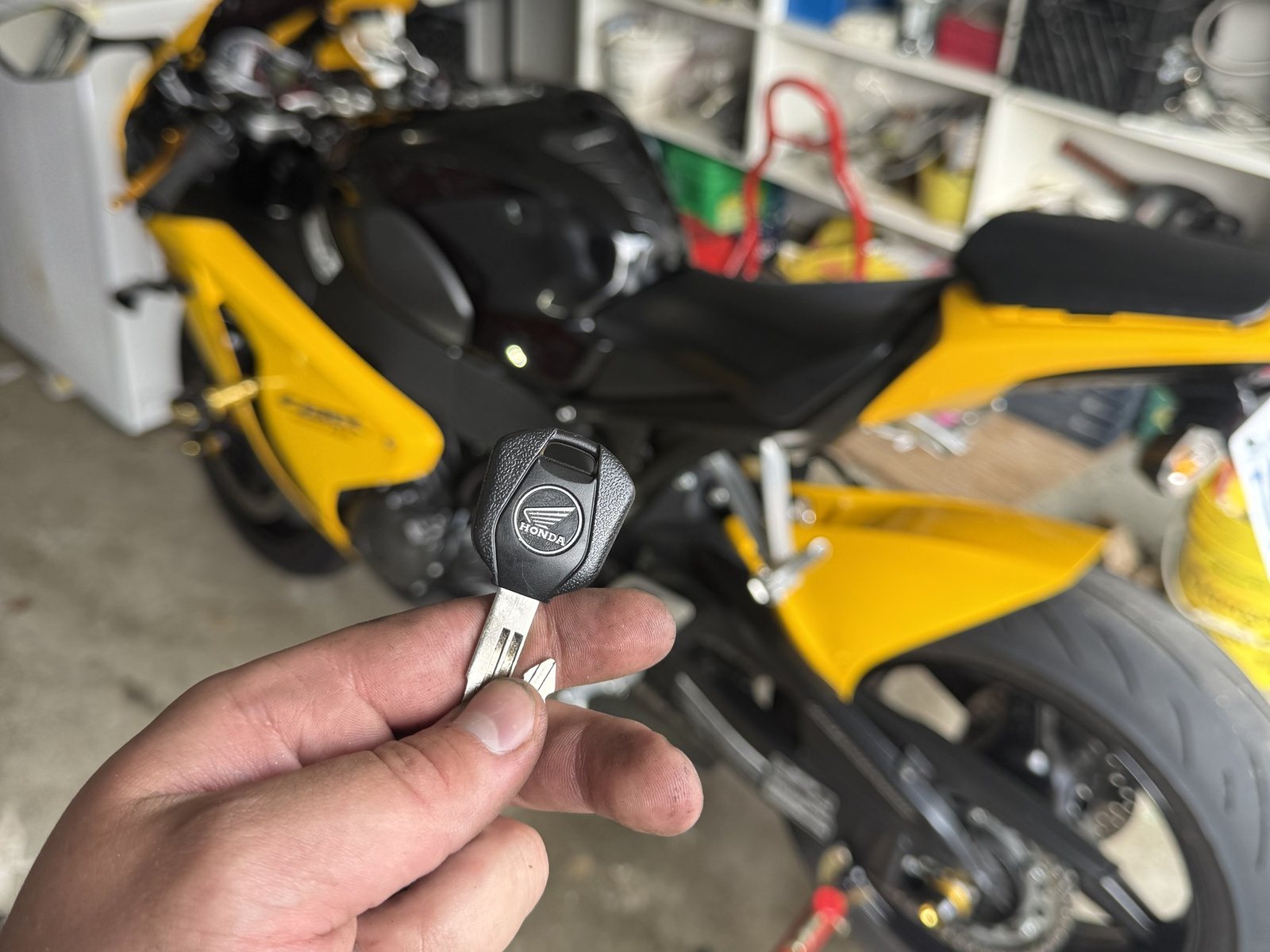 Yellow Honda sport motorcycle in a garage with a hand holding its Honda key