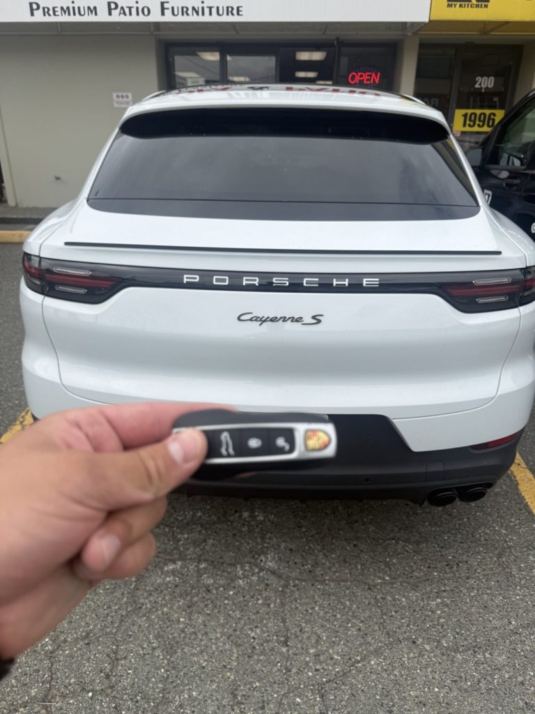 Hand holding a Porsche smart key behind a white Porsche Cayenne S in Vancouver