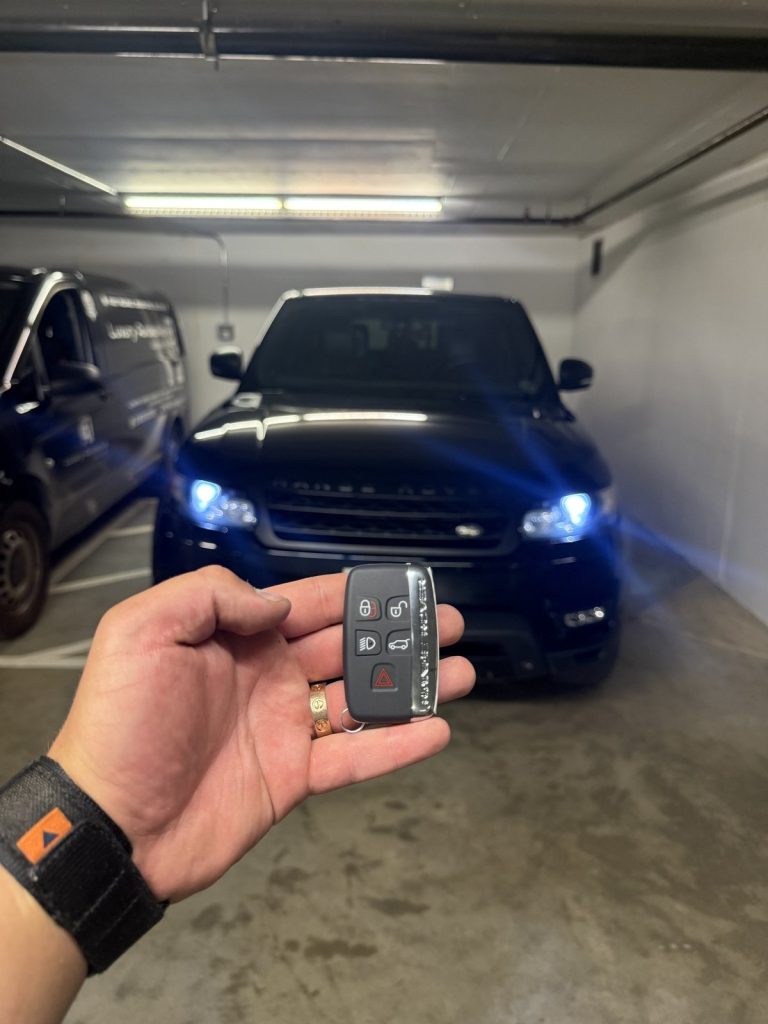Hand holding a Range Rover smart key in front of a dark Range Rover Sport in a Vancouver parkade
