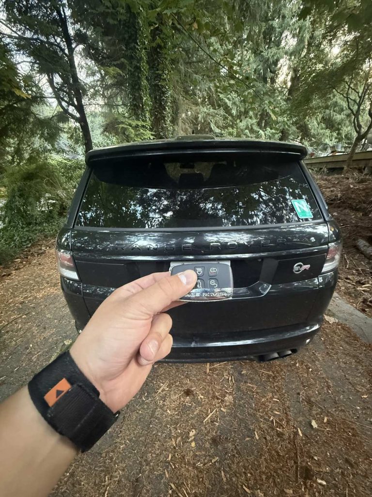 Hand holding a Range Rover key fob at the tailgate of a black Range Rover Sport SVR in Vancouver