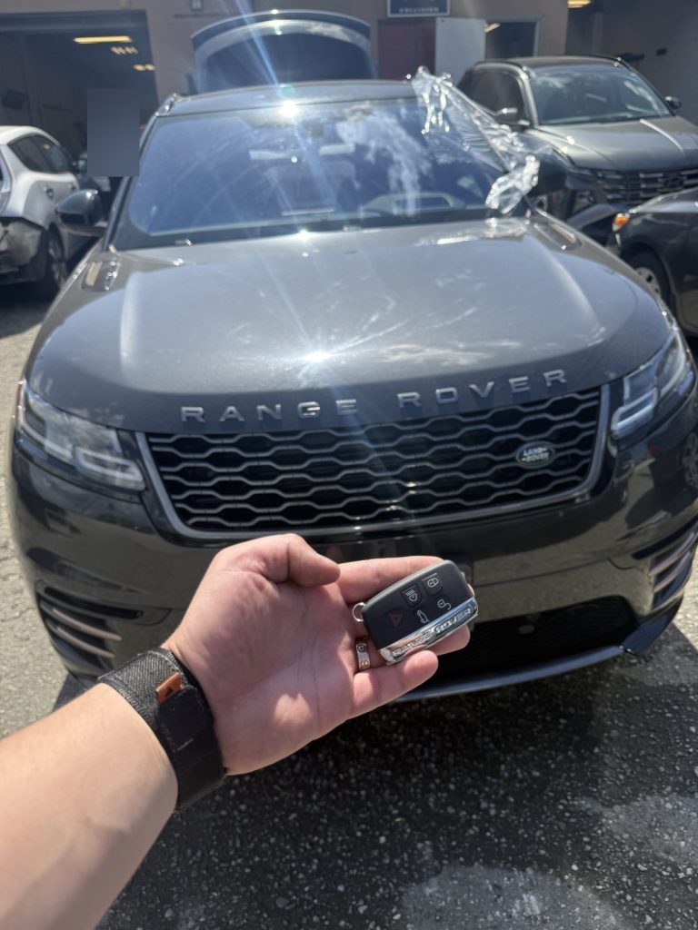 Hand holding a Range Rover key fob in front of a dark grey Range Rover Velar in Vancouver