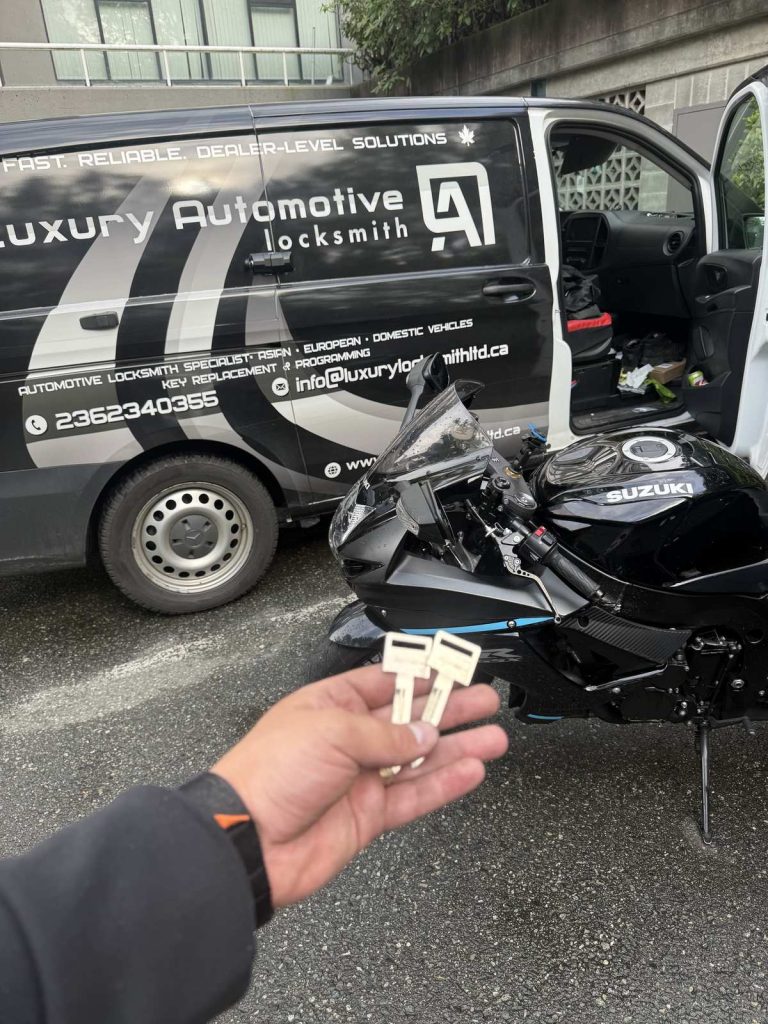 Two motorcycle keys held in front of a black Suzuki sport motorcycle beside the Luxury Automotive Locksmith van in Vancouver