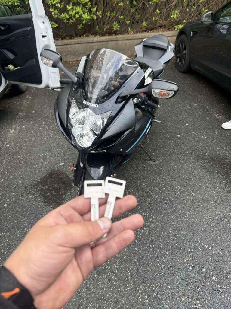 Hand holding two cut motorcycle keys in front of a black Suzuki sport motorcycle in Vancouver