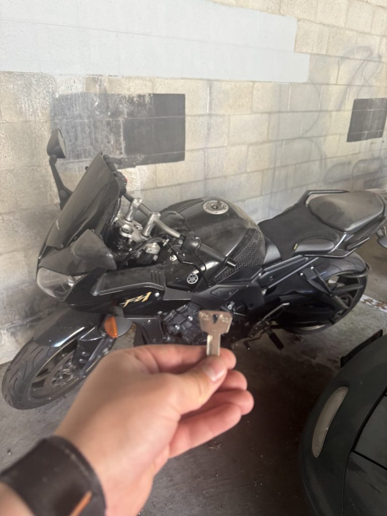 Hand holding a cut motorcycle key beside a black Yamaha motorcycle in a Vancouver parkade
